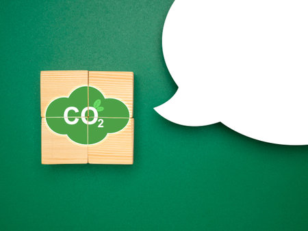 Green industries business and CO2 emission concept. Wooden cubes with CO2 green icons and a blank white speech bubble over a green background. Renewable energy. Space for text. Top viewの写真素材