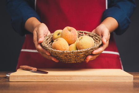 Chef carrying a basket with ripe peaches fruit while standing in the kitchen. Healthy fruit and food concept. Close-up photoの写真素材