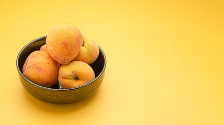 Fresh peaches fruit on a bowl over a yellow background. Top view. Close-up photo. Space for text. Healthy food and fruit conceptの写真素材
