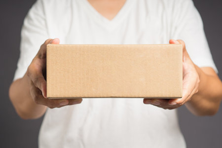 Man in white casual holding a cardboard box while standing on a gray background