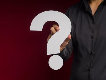 Question mark symbol concept. Businessman holding a white question mark paper while standing over a red background in the studio. Close-up photo. Space for textの写真素材