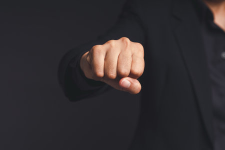 A businessman in a black suit raises his fist to the front, showing determination, and encouragement while standing on a black background. Business and fighting obstacles conceptの写真素材