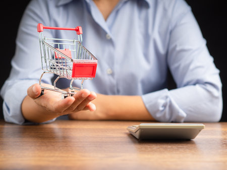 A mini shopping trolley on the palm of a businesswoman while sitting on a black background. Business and e-Commerce conceptの写真素材