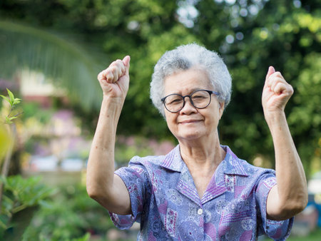Happy elderly Asian woman hands up before exercising over green nature at park outdoor. Aged people and exercise conceptの写真素材