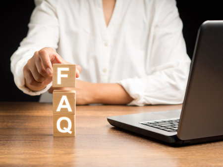 FAQs. A list of answers to Frequently Asked Questions. Hand holding a wooden cube with letters FAQ on a wooden desk in the office. Close-up photoの写真素材