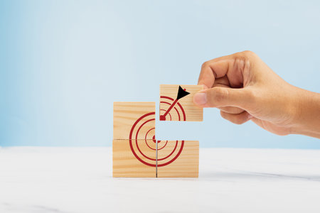 Concept of business achieving goal. Focus on a goal and achieve a successful business. Darts target icon on wooden cubes on the marble floor with a light blue backgroundの写真素材