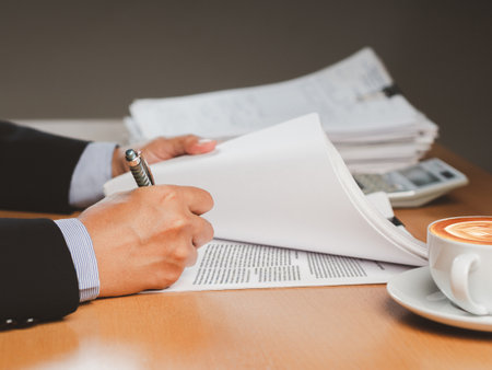 Close-up of a businessman signing on documents while sitting working in the office. Company executive, business owner, employer signing contract, agreement, paper report at workplaceの写真素材