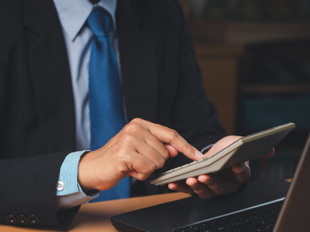 Close-up of a businessman in a suit sitting working in the office using a calculator to calculate the numbers. Finance and accounting concept. Close-up photoの写真素材
