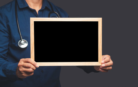 Close-up of hand a doctor holding a blank mini blackboard while standing on a gray background. Space for text. Medical and announcement conceptの写真素材