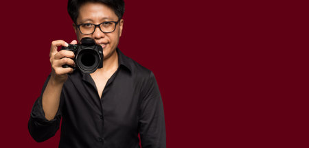 Photographer with a camera. A person is holding the digital camera while standing on a red background.の写真素材