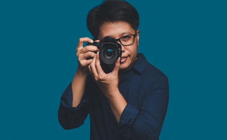 A Photographer holding a digital camera while standing on a blue background.の写真素材