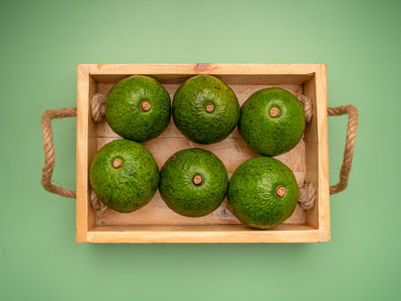Avocados in a wooden tray on a green background. Top view. Close-up photo. Healthy fruits conceptの写真素材