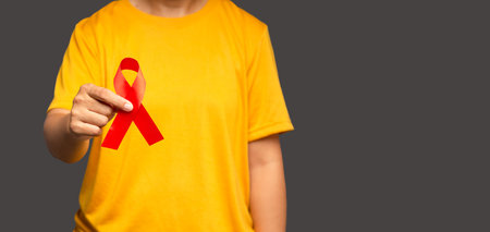 Hand holding a red ribbon for December World AIDS Day while standing on a gray background. Healthcare and safe sex concept. Space for textの写真素材
