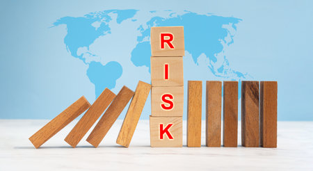 Risk management and strategy in business concept. Close-up of wooden blocks on a line of dominos over a marble floor with a world map and blue backgroundの写真素材