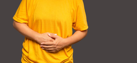 A woman suffering from abdominal pain used her hand to hold her belly while standing on an orange background. Stomach pain causes gastric ulcers, period cramps, or gastrointestinal system diseaseの写真素材