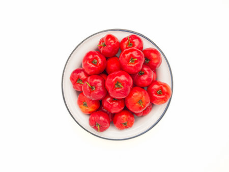 Top view of ripe red acerola cherries on a white dish over a white background. High vitamin C and antioxidant fruits. Space for text. Close-up photo. Healthy fruits conceptの写真素材