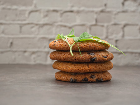 Close-up of cannabis chocolate chip cookies with a marijuana leaf on white brick wall background. Treatment of medical marijuana for use in food. Concept of cooking with cannabis herbの写真素材