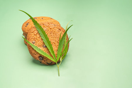 Cannabis chocolate chip cookies with a marijuana leaf on a green background. Space for text. Treatment of medical marijuana for use in food. Concept of cooking with cannabis herb. Top viewの写真素材