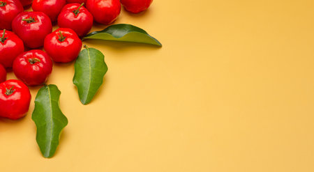 Top view of ripe red acerola cherries and green leaves on a yellow background. High vitamin C and antioxidant fruits. Space for text. Close-up photo. Healthy fruits conceptの写真素材