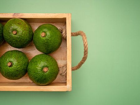 Avocados in a wooden tray on a green background. Top view. Close-up photo. Healthy fruits concept