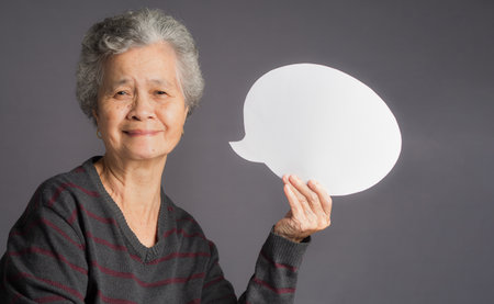 Speech bubble concept. An elderly Asian woman in a sweater with short gray hair holding a blank...