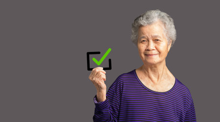 Senior woman holding a green check mark symbol with a black border and looking at the camera with a...