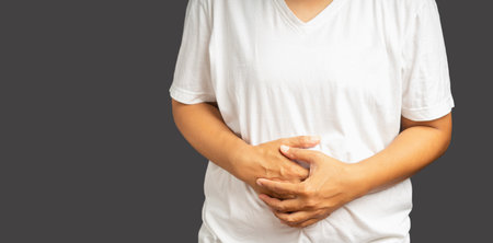 A woman suffering from abdominal pain used her hands to hold his belly while standing on a gray...