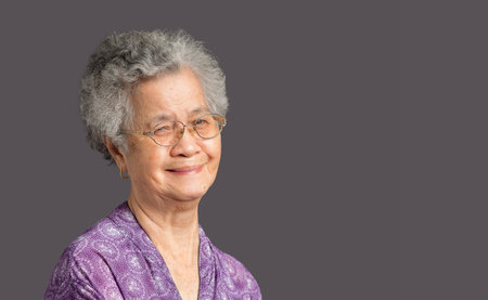 Portrait of an elderly Asian woman with short gray hair looking at the camera with a smile while...