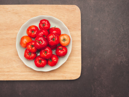 Ripe red acerola cherries on a white plate over a wooden cutting board. High vitamin C and...