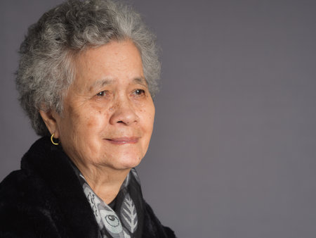 Portrait of an elderly Asian woman with short gray hair looking away with a smile while standing on...