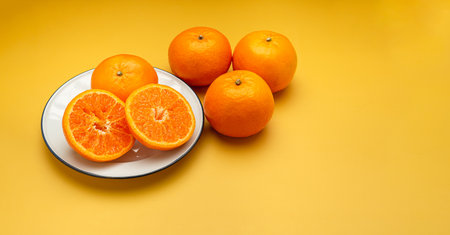 Pile of fresh oranges and half fruit on a white plate and yellow background with copy space for text. Healthy fruit concept. Close-up photoの写真素材