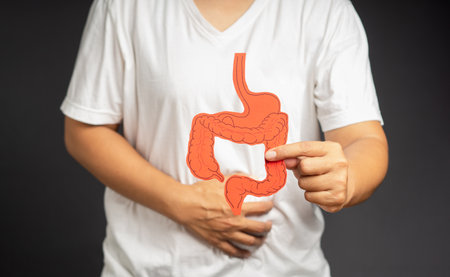 Close-up of hand holding a colon symbol and touching stomach painful suffering from stomach ache while standing on a gray backgroundの写真素材
