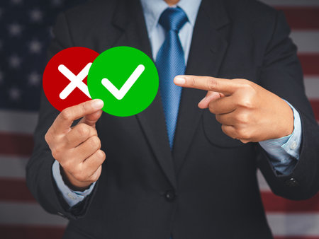 Close-up of hands businessman in a suit holding two papers with a checkmark and cross while standing on the background. True and false symbols accept rejected for evaluation. Yes or Noの写真素材