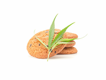 Cannabis chocolate chip cookies with a marijuana leaf on a white background. Concept of cooking with cannabis herbの写真素材