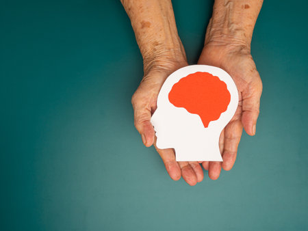 Top view of head with a brain made from paper on the palm senior woman over a green background. Awareness of Alzheimer's, Parkinson's, dementia, stroke, seizure, or mental health. Space for textの写真素材