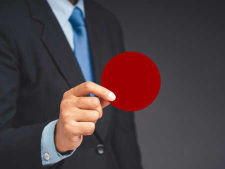 Close-up of hand businessman in a suit holding a blank red circle paper while standing on a gray background. Space for textの写真素材