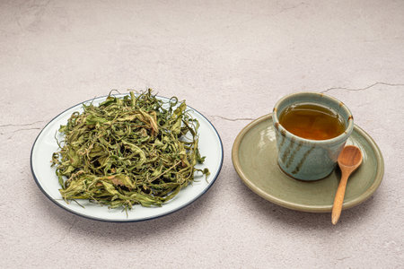 Dry cannabis leaf tea on a white plate and marijuana tea cup on a table. Textured marijuana leaves. Concept of beverage with cannabis herbの写真素材