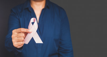 Breast cancer awareness concept. Woman in a blue shirt with a hand holding a pink ribbon for cancer patient support. Healthcare, International Women's Day, and World cancer day conceptの写真素材