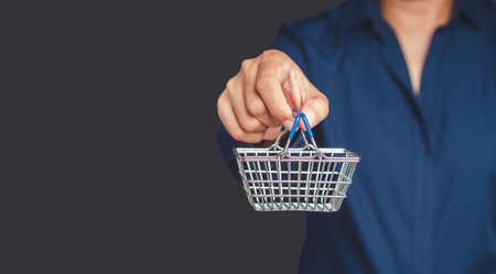 A young man is holding a mini shopping cart while standing on a gray background. Concept of online...