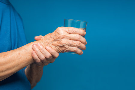 Close-up of hands senior woman trying to hold a glass of water. Causes of handshaking include Parkinson's disease, stroke, or brain injury. Mental health neurological disorderの写真素材
