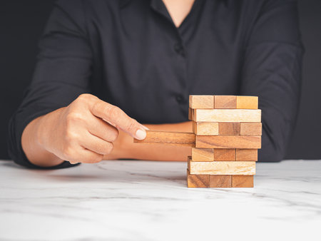 Risk of management and strategy plans for business growth and success concept. Close-up hand of a man playing a wooden block game while sitting at the tableの写真素材