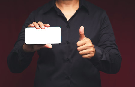 Midsection of a businessman holding a horizontal mobile phone with a blank white screen and showing...