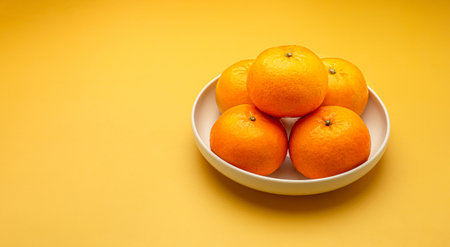 Top view of fresh oranges on a white plate over a yellow background. Healthy fruit concept. Close-up...