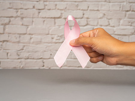 Breast cancer awareness concept. Close-up of hand holding a pink ribbon for cancer patient support....
