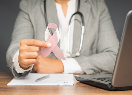 Breast cancer awareness concept. A doctor hand holding a pink ribbon for cancer patient support while sitting in the hospital.の写真素材
