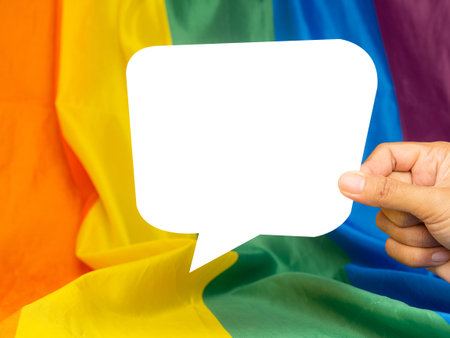 Hand holding a white speech bubble on the rainbow flag or LGBT flag background. Space for text....
