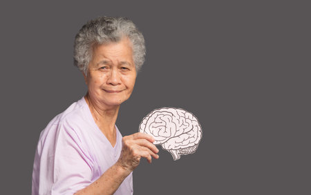 Portrait of a senior woman holding a brain symbol while standing on a gray background. Alzheimer's, Parkinson's, dementia, stroke, seizure, or mental health. Medical and healthcare conceptの写真素材