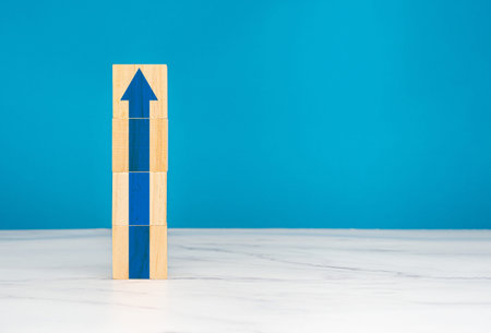 Business growth concept. Wooden cubes stacked with blue arrows up with a blue background. Space for...