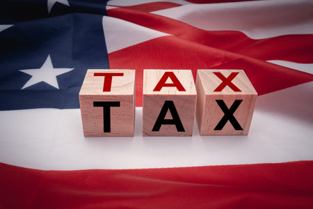 Wooden cubes with letters TAX on the American flag background. Tax payment and individual income tax return. Accounting and Taxes conceptの写真素材