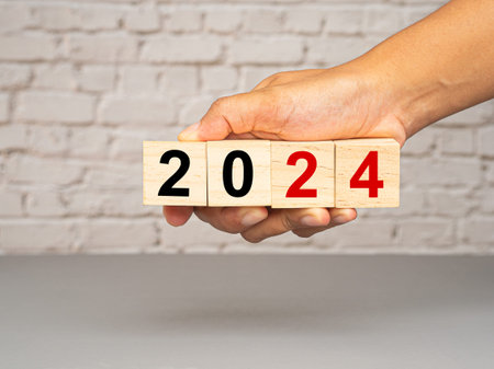 Countdown and business planning in 2024. Hand holding of wooden cubes with the letters 2024 with a white brick wall background. New year's eve and change the year 2023 to 2024の写真素材